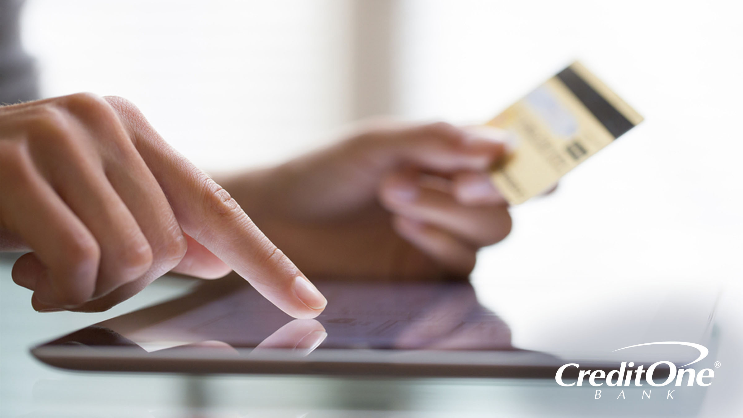 A person’s right hand taps on a tablet, while their left hand holds a credit card. They may be safely shopping online with their credit card after taking the right precautions.